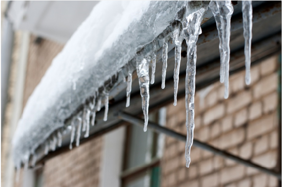 Large icicles hanging from the edge of a snow-laden roof.