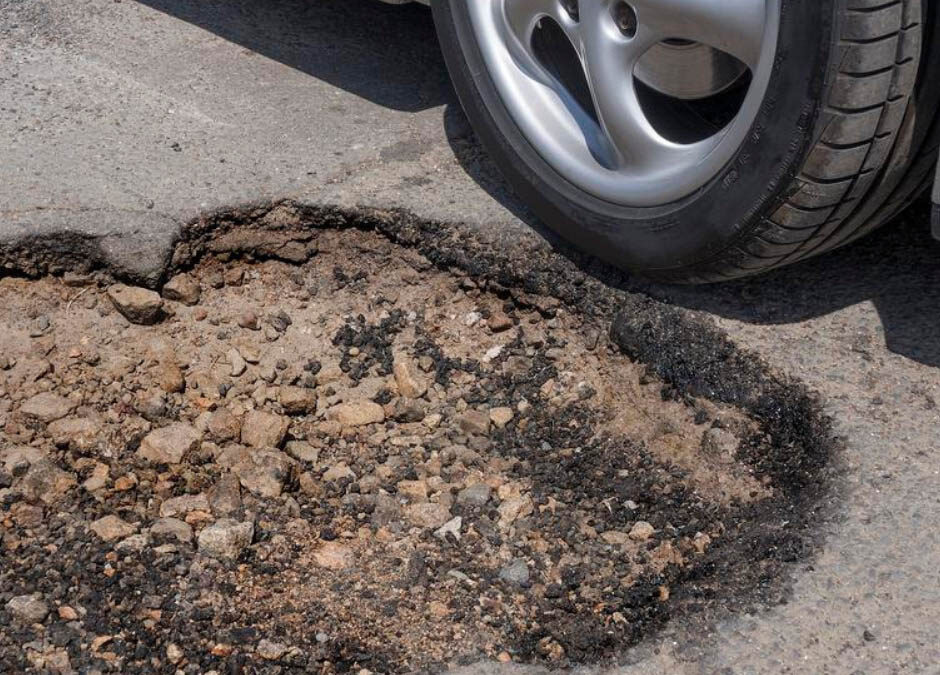 A pothole on a paved road beside a car tire